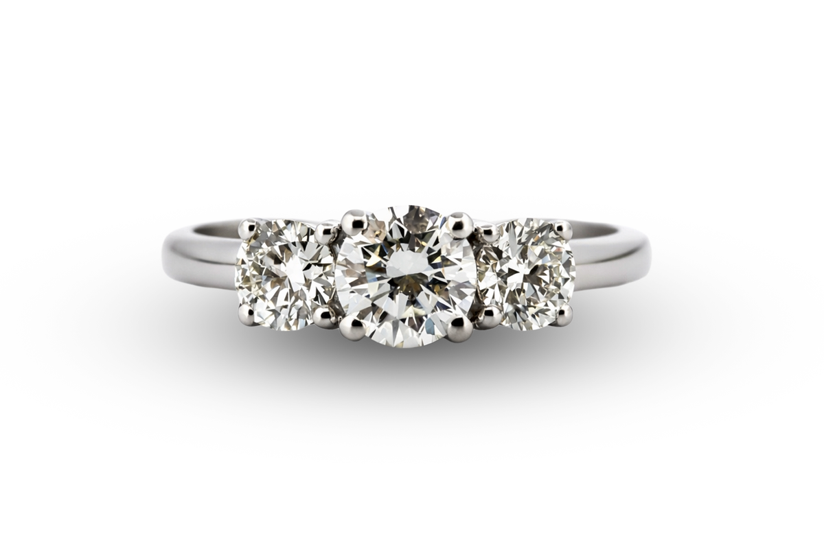 A three-stone diamond ring in a silver-colored metal setting, featuring a round center stone flanked by two round side stones, shown on a plain white background.