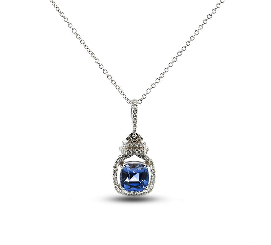 A silver pendant necklace featuring a cushion-cut blue sapphire gemstone surrounded by small clear accent stones, suspended from a delicate silver chain on a white background.