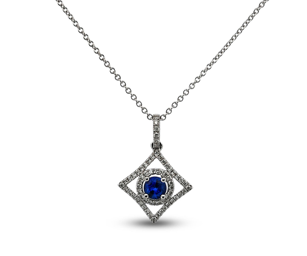 A silver-toned diamond pendant necklace featuring a central round-cut deep blue sapphire surrounded by a halo of small diamonds, set within a larger diamond-shaped frame on a delicate chain.